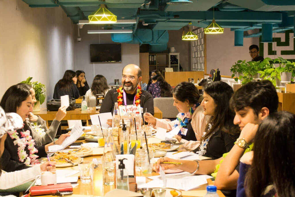 A Game Master explaining a game to a full table of guests at Unwind